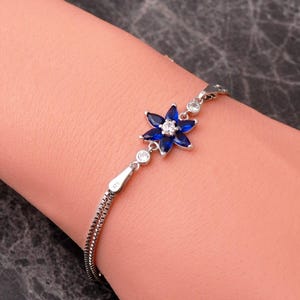 A delicate 925 sterling silver bracelet featuring a centrally placed lotus flower motif set with a brilliant gemstone, attached to a fine chain with an extension link.