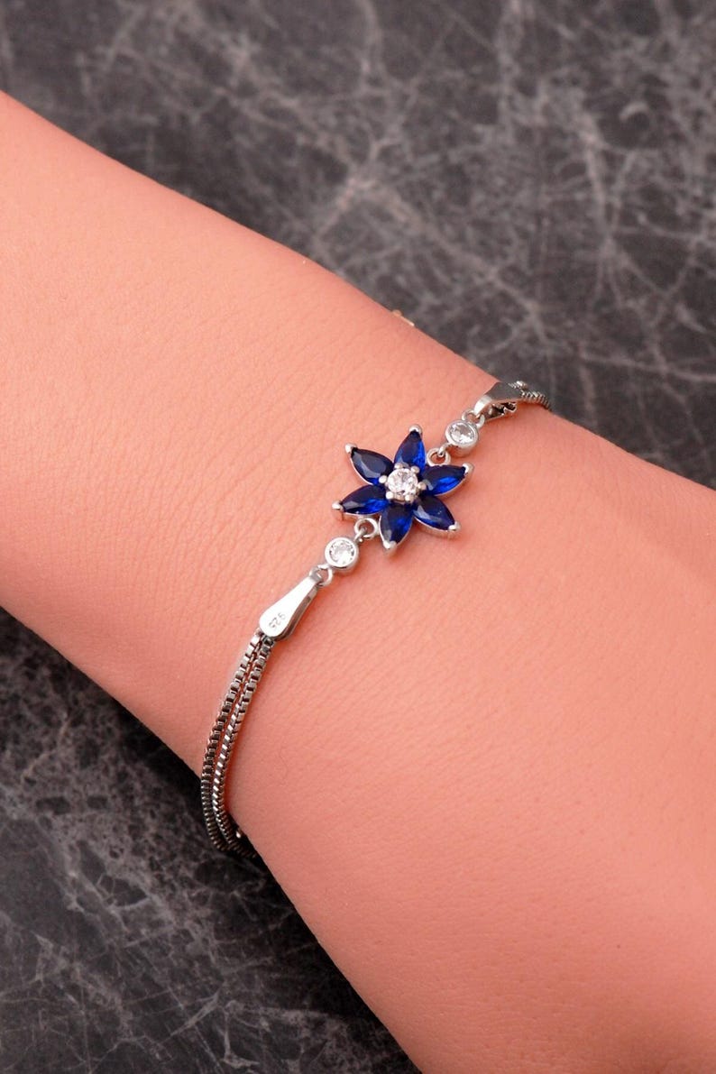 A delicate 925 sterling silver bracelet featuring a centrally placed lotus flower motif set with a brilliant gemstone, attached to a fine chain with an extension link.