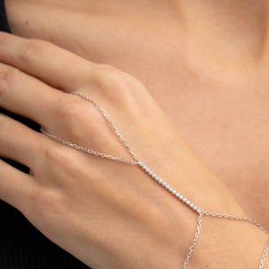 A sparkling 925 sterling silver hand harness bracelet featuring clear cubic zirconia tennis stones that wraps twice around the wrist and connects elegantly to a finger ring.