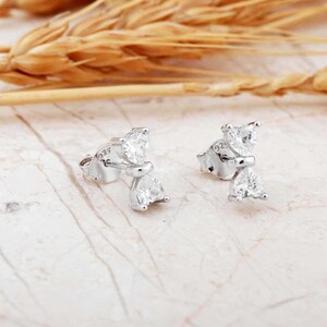 Mini bow‑shaped earrings made of rhodium‑plated sterling silver with a single white zircon stone on each side, measuring 4 mm tall by 1 cm wide.