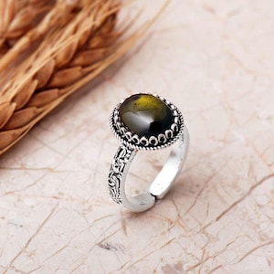 Adjustable oval ring made of 925 sterling silver with a green peridot stone on one side and a purple amethyst stone on the other, showing an oxidized antique finish.
