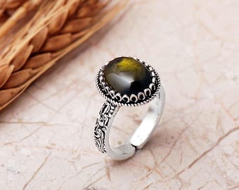 May include: A silver-toned ring featuring an oval-shaped, dark green gemstone set in a decorative, rope-textured bezel. The band displays an intricate, embossed pattern along its outer surface and includes an open, adjustable gap.