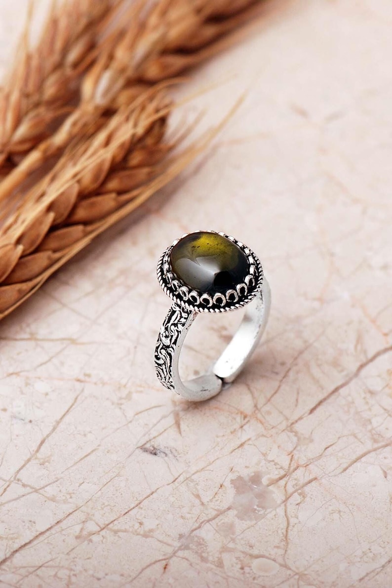 Adjustable oval ring made of 925 sterling silver with a green peridot stone on one side and a purple amethyst stone on the other, showing an oxidized antique finish.