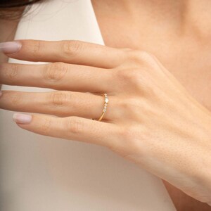 A close‑up of a thin silver ring with green gold plating and sparkling zircon stones, featuring a larger 2.5 mm center stone and smaller 1.5 mm accents.