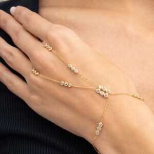 A gold-plated 925 sterling silver hand harness bracelet featuring delicate chains connecting a finger ring to a wrist bracelet embellished with sparkling round clear zircon gemstones.