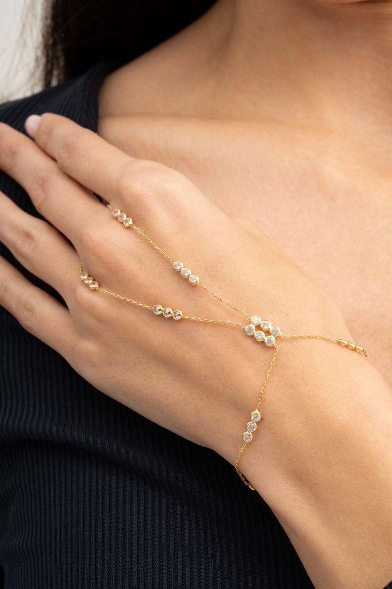 A gold-plated 925 sterling silver hand harness bracelet featuring delicate chains connecting a finger ring to a wrist bracelet embellished with sparkling round clear zircon gemstones.