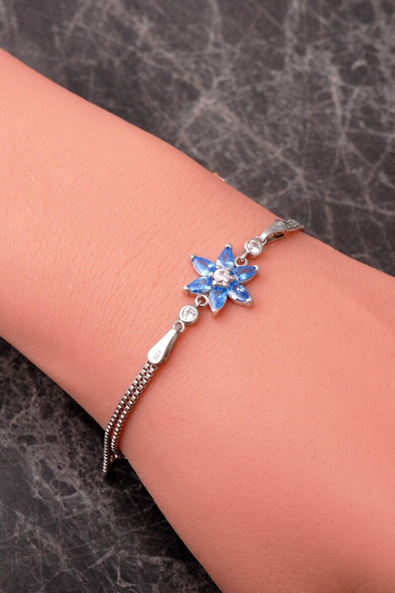A delicate 925 sterling silver bracelet featuring a centrally placed lotus flower motif set with a brilliant gemstone, attached to a fine chain with an extension link.