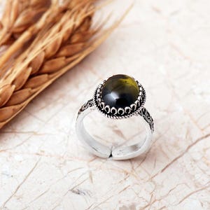 Adjustable oval ring made of 925 sterling silver with a green peridot stone on one side and a purple amethyst stone on the other, showing an oxidized antique finish.