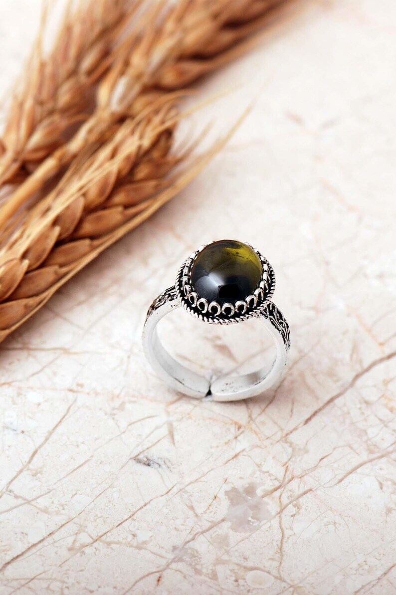 Adjustable oval ring made of 925 sterling silver with a green peridot stone on one side and a purple amethyst stone on the other, showing an oxidized antique finish.