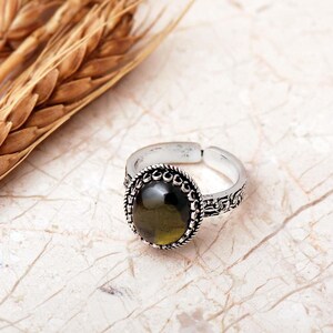 Adjustable oval ring made of 925 sterling silver with a green peridot stone on one side and a purple amethyst stone on the other, showing an oxidized antique finish.