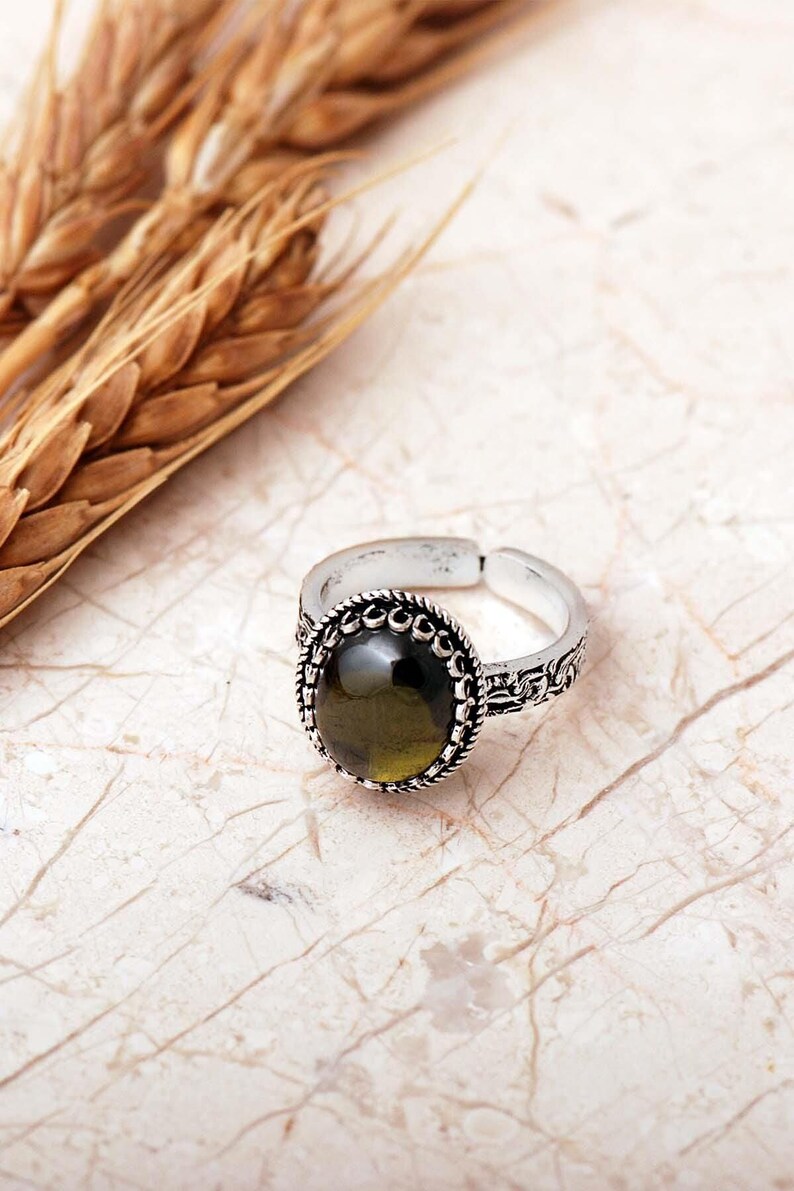 Adjustable oval ring made of 925 sterling silver with a green peridot stone on one side and a purple amethyst stone on the other, showing an oxidized antique finish.