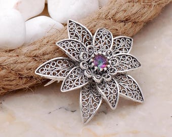 May include: A silver filigree flower brooch with a iridescent purple and pink gemstone in the center.
