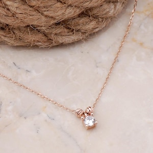 Op de afbeelding: Een roségouden ketting met een ronde, heldere edelsteen als hanger. De hanger wordt geflankeerd door twee kleine, getextureerde roségouden kraaltjes en de fijne ketting is voorzien van een standaard sluiting.