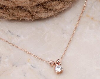 May include: A rose gold chain necklace featuring a single round clear gemstone pendant. The pendant is flanked by two small, textured rose gold beads, and the delicate chain is secured with a standard clasp mechanism.