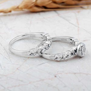 A pair of white rhodium‑plated sterling silver rings; the larger solitaire features a clear zircon stone, and the slimmer band complements it with a sleek design.