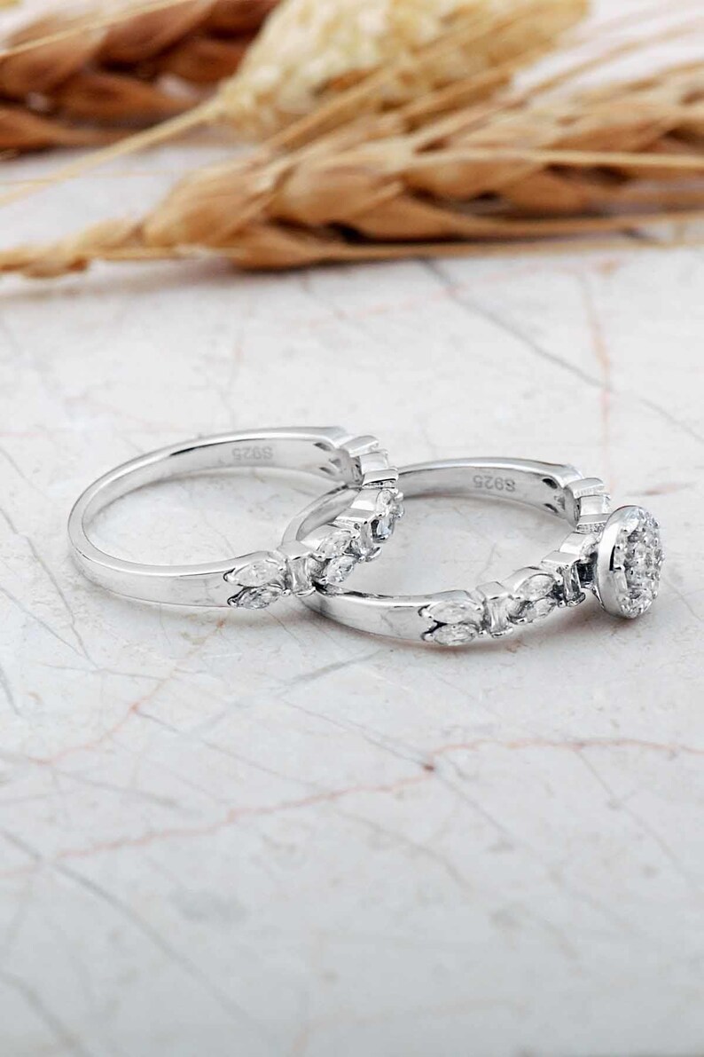 A pair of white rhodium‑plated sterling silver rings; the larger solitaire features a clear zircon stone, and the slimmer band complements it with a sleek design.