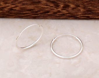 May include: A pair of small, polished silver hoop earrings. Each earring features a thin, circular wire design with a simple hinged closure mechanism, showcasing a bright, reflective metallic finish that catches the light evenly across the surface.