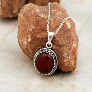May include: A silver chain necklace with a red gemstone pendant. The pendant is round and has a silver filigree design around the edge.