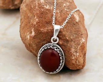 May include: A silver chain necklace with a red gemstone pendant. The pendant is round and has a silver filigree design around the edge.