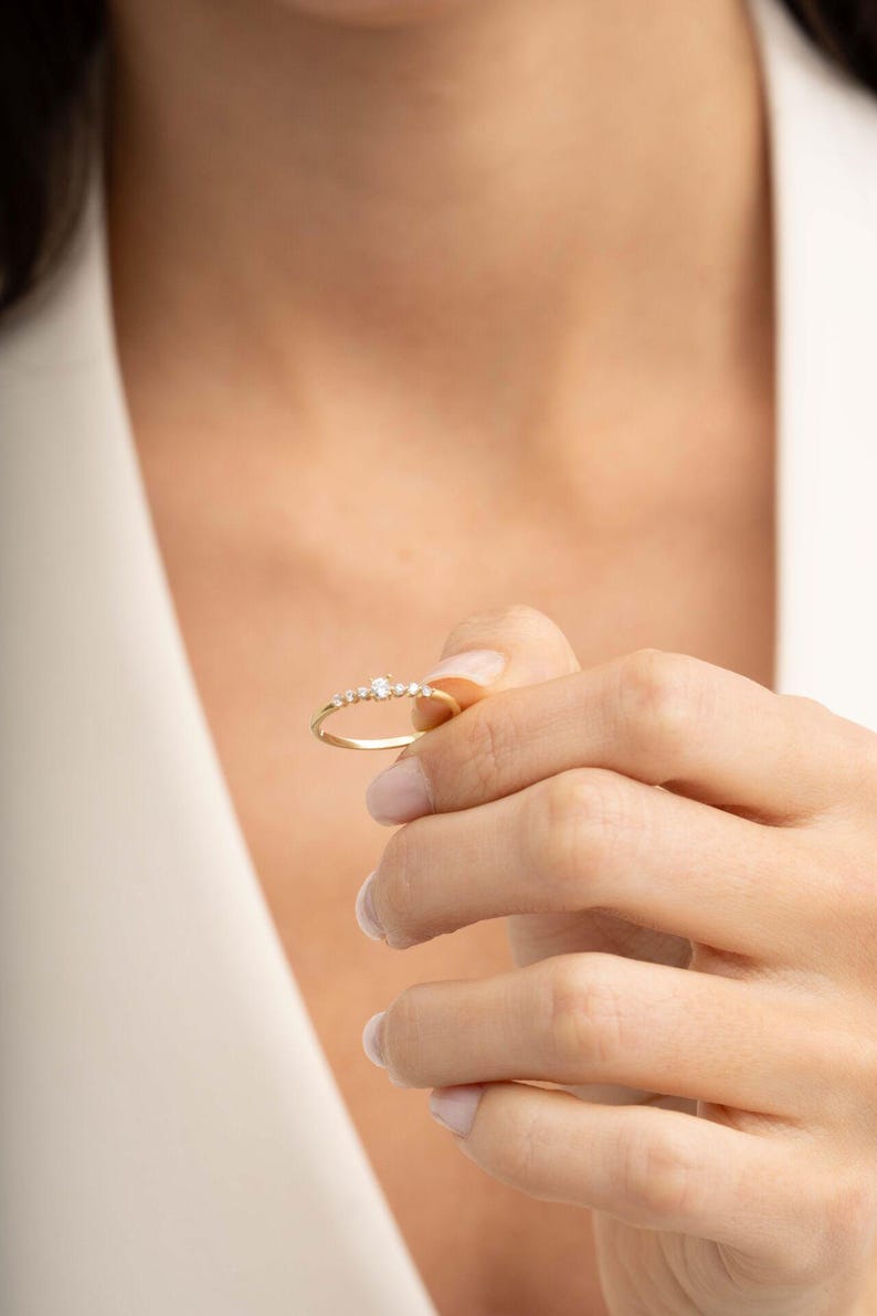 A close‑up of a thin silver ring with green gold plating and sparkling zircon stones, featuring a larger 2.5 mm center stone and smaller 1.5 mm accents.