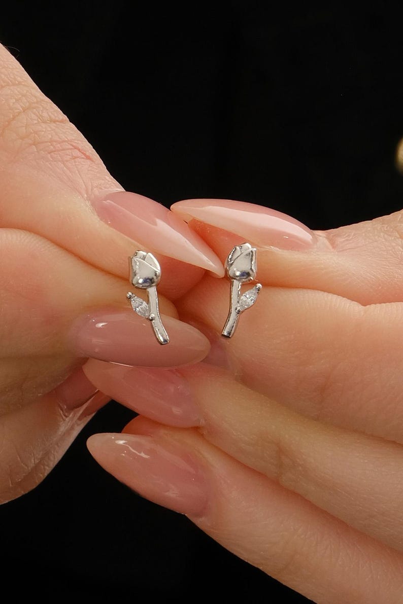 A pair of small silver earrings featuring a minimalist tulip shape adorned with sparkling white zircon stones, rhodium‑plated for a bright finish.