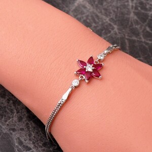 A delicate 925 sterling silver bracelet featuring a centrally placed lotus flower motif set with a brilliant gemstone, attached to a fine chain with an extension link.