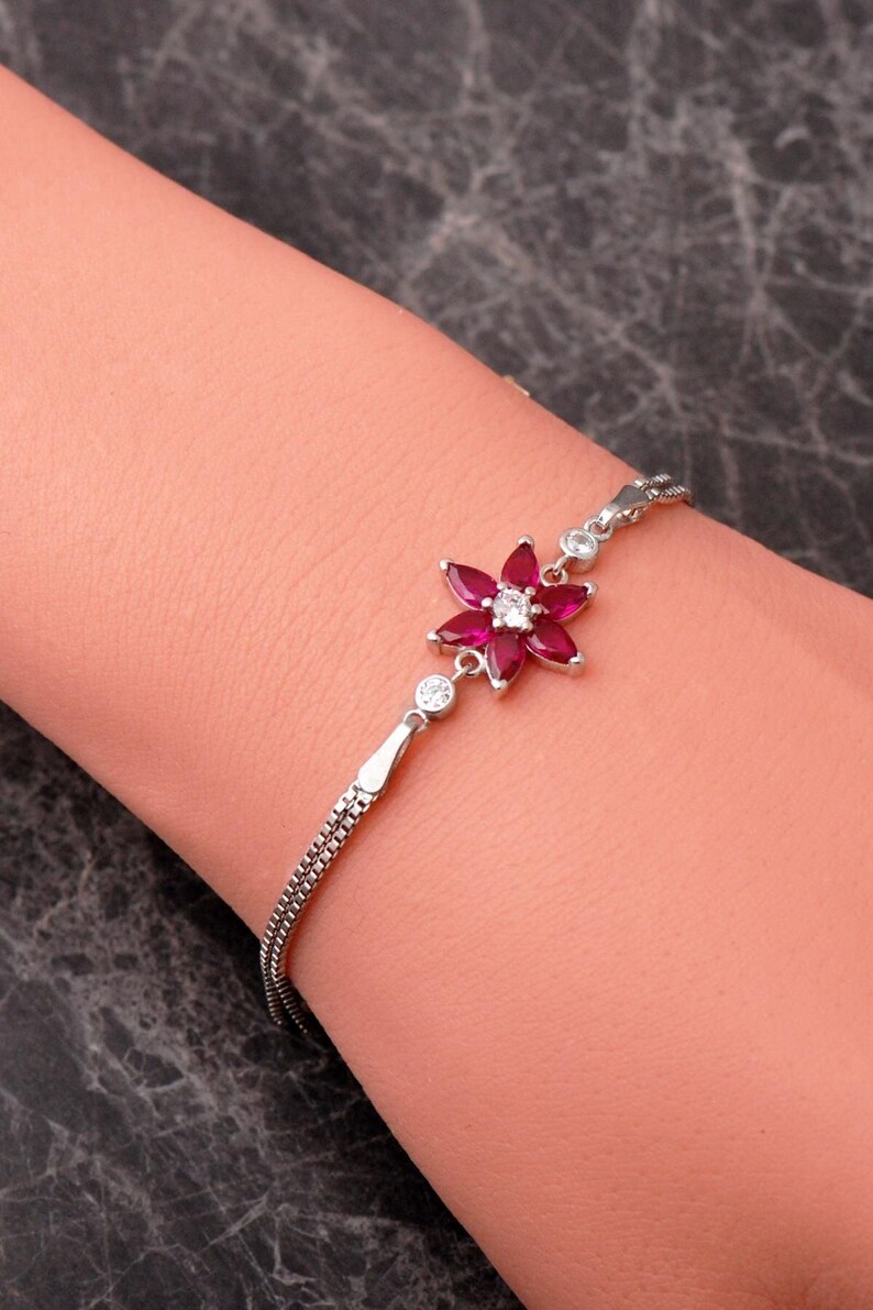 A delicate 925 sterling silver bracelet featuring a centrally placed lotus flower motif set with a brilliant gemstone, attached to a fine chain with an extension link.