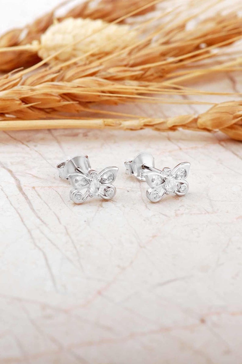 Mini butterfly earrings made of rhodium‑plated sterling silver with a white zircon stone, measuring 6 mm by 9 mm.