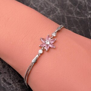 A delicate 925 sterling silver bracelet featuring a centrally placed lotus flower motif set with a brilliant gemstone, attached to a fine chain with an extension link.