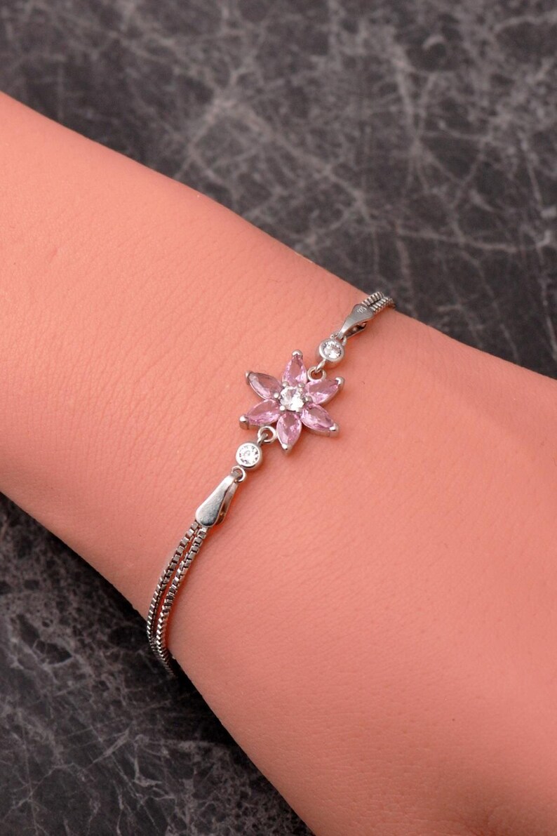 A delicate 925 sterling silver bracelet featuring a centrally placed lotus flower motif set with a brilliant gemstone, attached to a fine chain with an extension link.