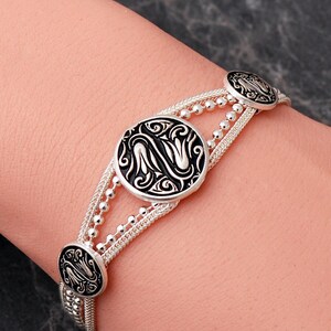 A handcrafted 925 sterling silver woven mesh bracelet featuring circular silver medallions decorated with black enamel tulip motifs and an adjustable lobster claw clasp.