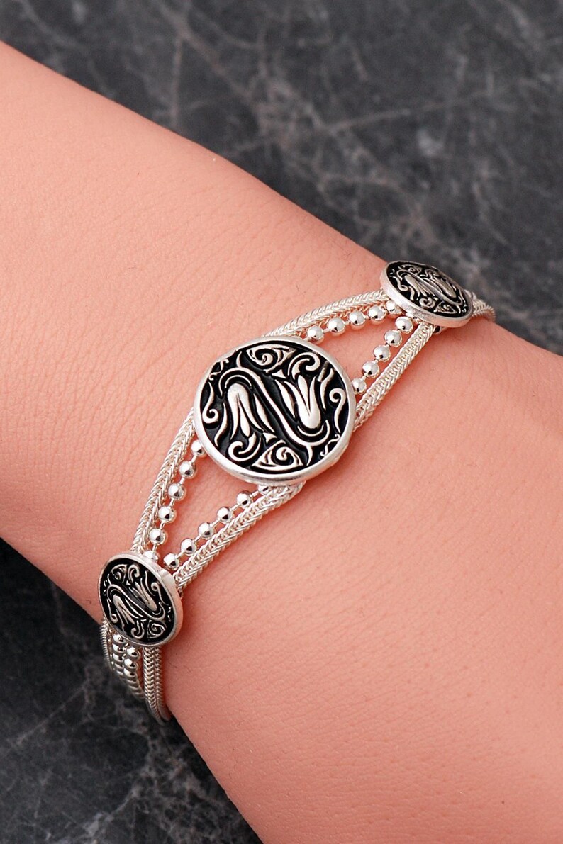 A handcrafted 925 sterling silver woven mesh bracelet featuring circular silver medallions decorated with black enamel tulip motifs and an adjustable lobster claw clasp.
