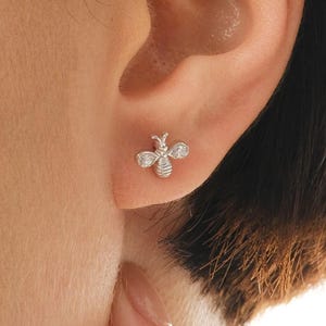 A pair of tiny 925 sterling silver bee stud earrings embellished with sparkling white cubic zirconia stones.