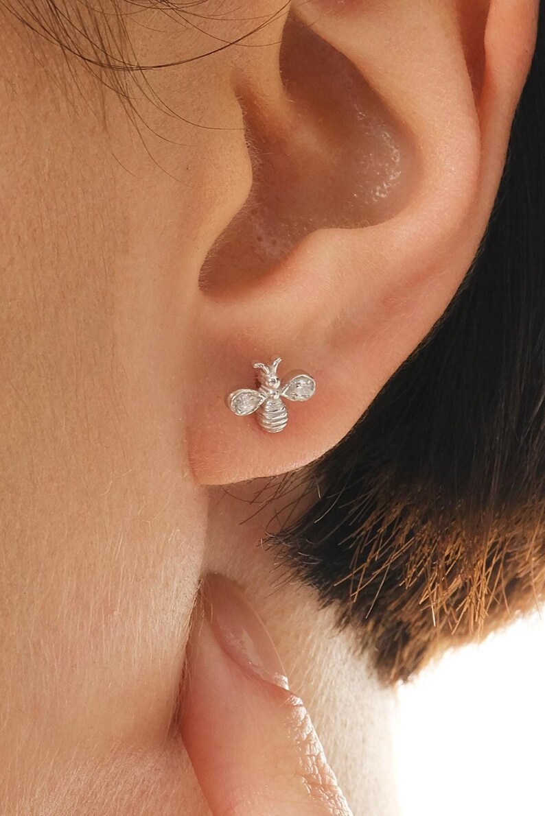 A pair of tiny 925 sterling silver bee stud earrings embellished with sparkling white cubic zirconia stones.