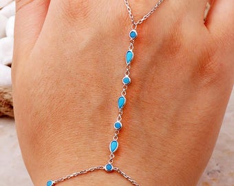 May include: A silver-toned hand chain bracelet featuring a delicate metal link chain adorned with small, alternating round and teardrop-shaped bright turquoise blue stones. The jewelry piece connects a wrist bracelet to a single finger ring.