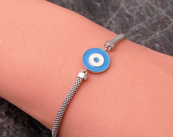 May include: A silver-toned bracelet featuring a central circular charm with concentric rings of light blue, white, and a smaller light blue center. The bracelet band is constructed from a fine, textured metallic mesh chain.