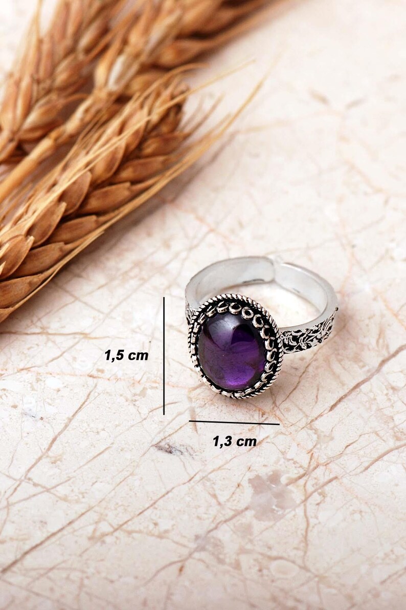 Adjustable oval ring made of 925 sterling silver with a green peridot stone on one side and a purple amethyst stone on the other, showing an oxidized antique finish.