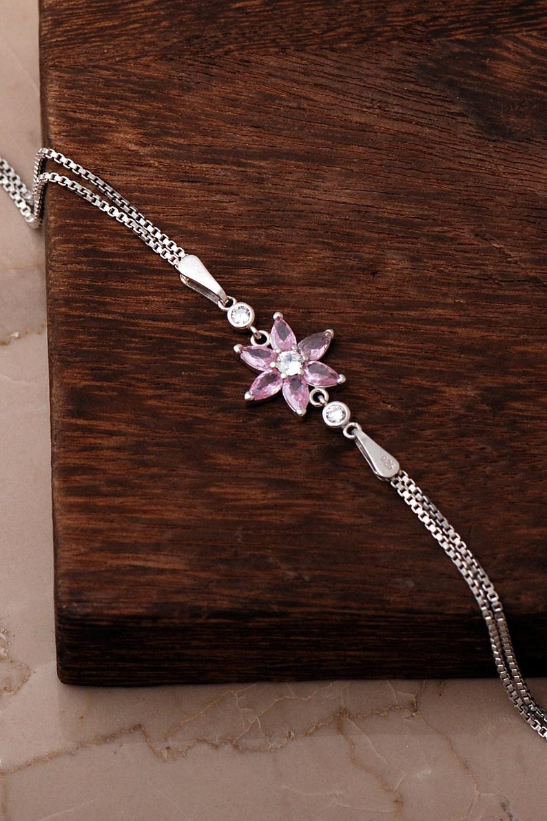 A delicate 925 sterling silver bracelet featuring a centrally placed lotus flower motif set with a brilliant gemstone, attached to a fine chain with an extension link.