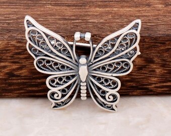 May include: A silver filigree butterfly brooch with intricate details. The brooch is delicate and ornate, with a detailed butterfly design.