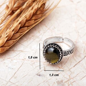 Adjustable oval ring made of 925 sterling silver with a green peridot stone on one side and a purple amethyst stone on the other, showing an oxidized antique finish.