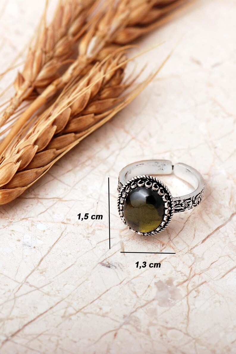 Adjustable oval ring made of 925 sterling silver with a green peridot stone on one side and a purple amethyst stone on the other, showing an oxidized antique finish.