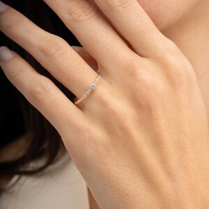A close‑up of a thin silver ring with green gold plating and sparkling zircon stones, featuring a larger 2.5 mm center stone and smaller 1.5 mm accents.