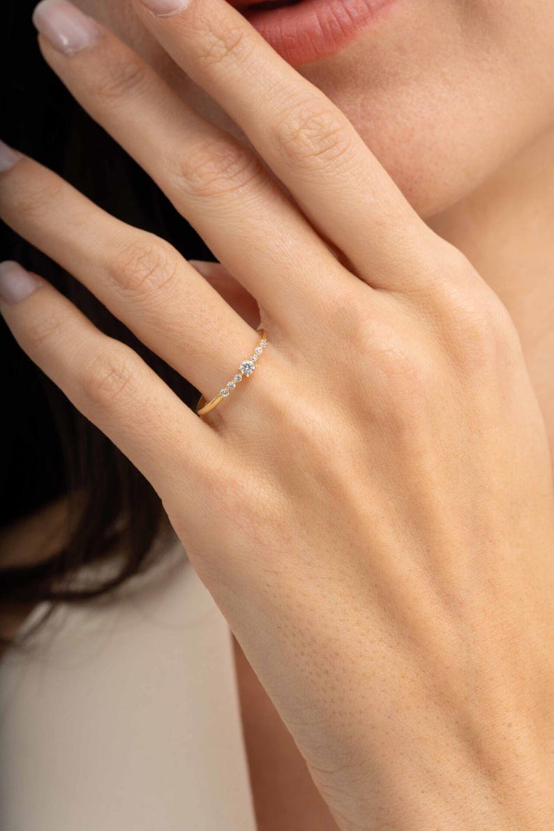 A close‑up of a thin silver ring with green gold plating and sparkling zircon stones, featuring a larger 2.5 mm center stone and smaller 1.5 mm accents.