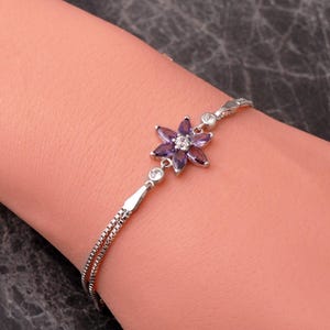 A delicate 925 sterling silver bracelet featuring a centrally placed lotus flower motif set with a brilliant gemstone, attached to a fine chain with an extension link.