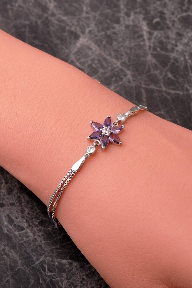 A delicate 925 sterling silver bracelet featuring a centrally placed lotus flower motif set with a brilliant gemstone, attached to a fine chain with an extension link.