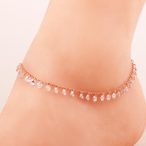 May include: A rose gold anklet featuring a delicate chain adorned with a series of small, clear, round-cut dangling crystals spaced evenly along the entire length of the metal chain, creating a shimmering effect around the ankle area.