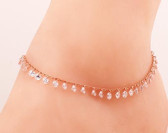 May include: A rose gold anklet featuring a delicate chain adorned with a series of small, clear, round-cut dangling crystals spaced evenly along the entire length of the metal chain, creating a shimmering effect around the ankle area.