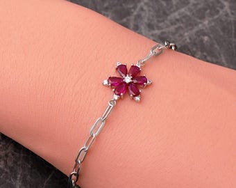 May include: A silver-toned chain bracelet featuring a central flower-shaped charm. The charm is composed of six pear-cut deep red stones arranged as petals around a small clear center stone, with additional clear stones accenting the flower base.