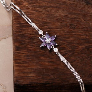 A delicate 925 sterling silver bracelet featuring a centrally placed lotus flower motif set with a brilliant gemstone, attached to a fine chain with an extension link.