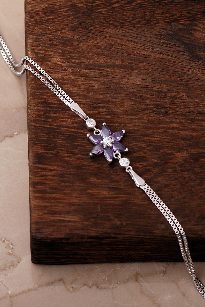 A delicate 925 sterling silver bracelet featuring a centrally placed lotus flower motif set with a brilliant gemstone, attached to a fine chain with an extension link.